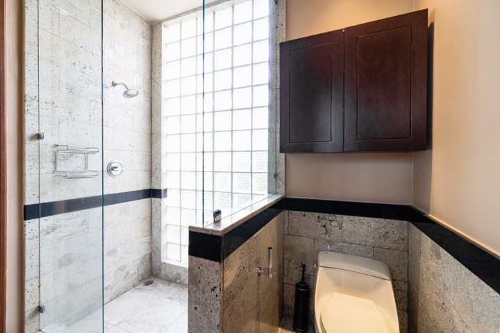 Modern bathroom with glass shower, stone walls, dark cabinet, and toilet.