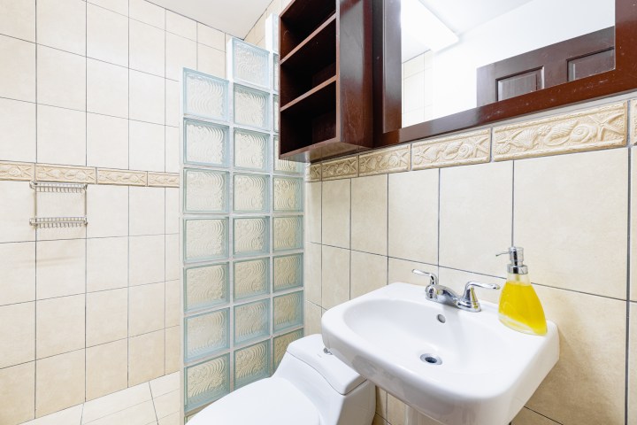 Bathroom with tile walls, glass block divider, sink, and yellow soap dispenser.
