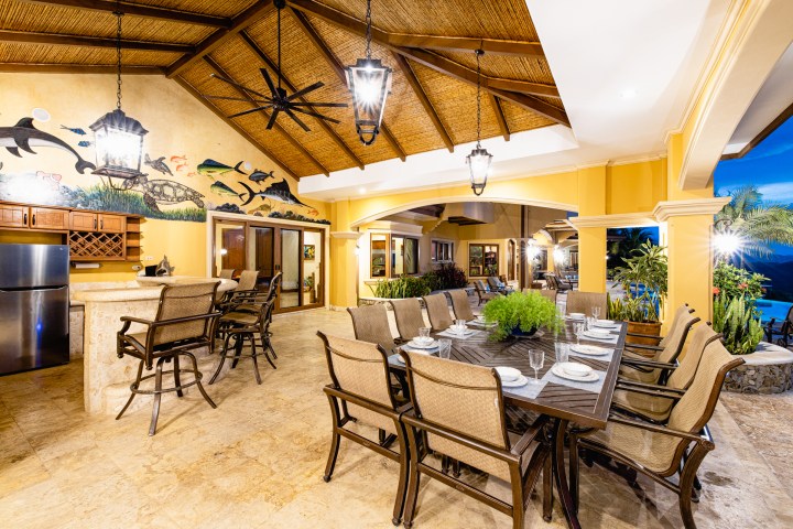 Covered outdoor dining area with decorative wall art and potted plants.