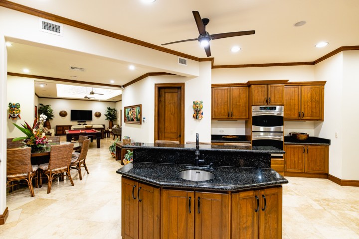 Spacious kitchen with wooden cabinets, marble counters, dining area, and living room with TV and pool table.
