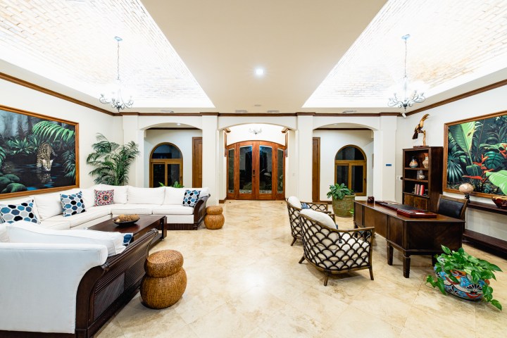 Spacious living room with white sofa, paintings, desk, and skylit ceiling.