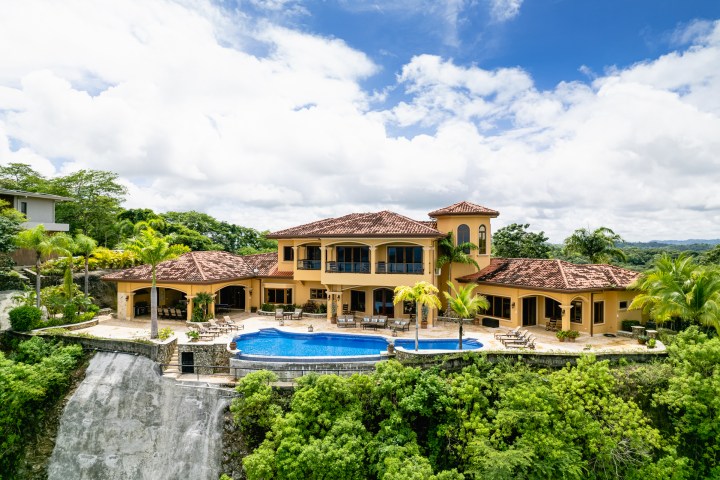 A luxury villa with a pool on a hillside, surrounded by lush greenery.