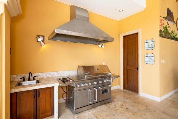 Outdoor kitchen with stainless steel grill, sink, and yellow walls.