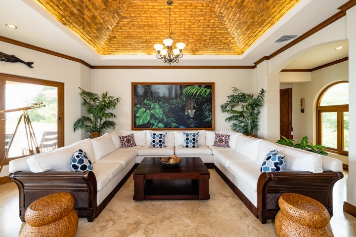 Elegant living room with white sofa, wood accents, large painting, plants, and telescope near a window.
