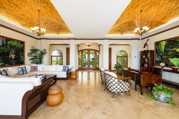 Spacious living room with white sofas, wooden desk, paintings, and large windows.