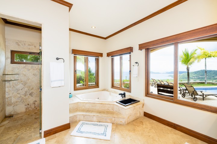 Luxurious bathroom with large windows, bathtub, and tropical garden view.