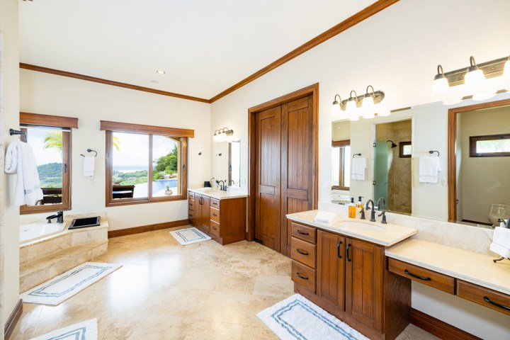 Spacious bathroom with wooden cabinets, dual sinks, bathtub, and large windows with a view.