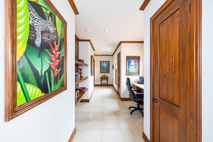 Bright hallway with nature paintings, wooden doors, and a desk with office chair.