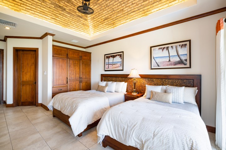 Bedroom with two beds, wood furniture, tropical paintings, and a brick ceiling.