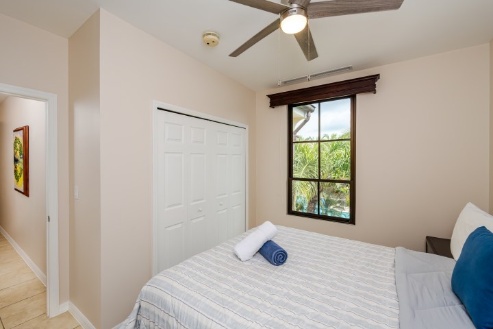 Bedroom with striped bedspread, window view, ceiling fan, and closet doors.