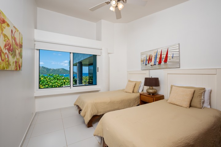 Bedroom with two beds, seascape view through window, sailboat and flamingo art on walls.
