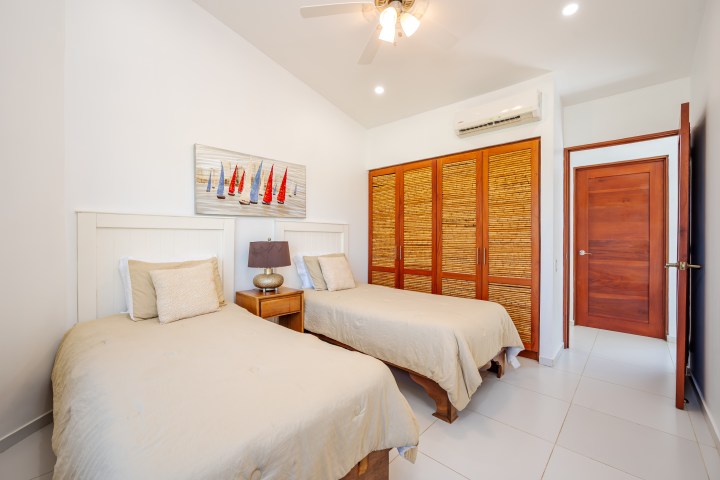 Two twin beds in a bright room with wooden closet and sailboat artwork.
