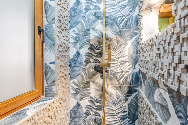Tropical-themed shower with gold fixtures, leaf-patterned walls, and textured tile accents.