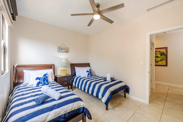 Two twin beds in a bright room with blue striped bedding and a ceiling fan.