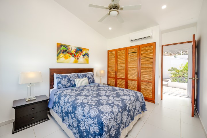 Bedroom with blue patterned bedding, wooden wardrobe, and colorful wall art.
