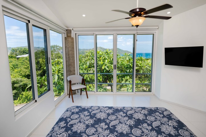 Bright room with large windows, ocean view, ceiling fan, chair, TV, and a patterned bedspread.