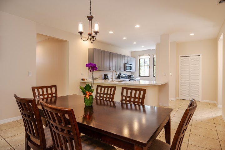 Dining room with wood table, chairs, orchid centerpiece, and view of modern kitchen.