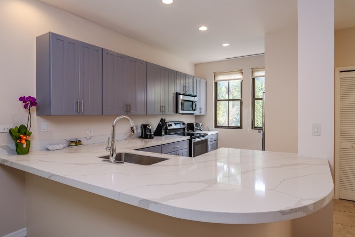 Modern kitchen with gray cabinets, marble countertops, and stainless steel appliances.