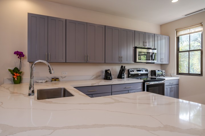 Modern kitchen with gray cabinets, stainless steel appliances, and marble countertops.