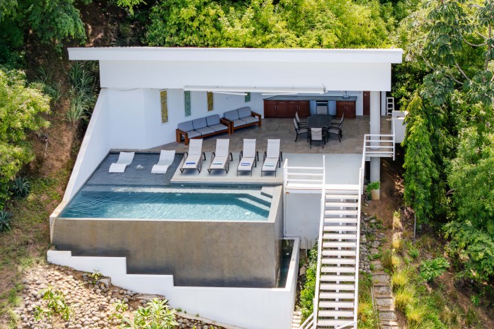 Outdoor pool with lounge chairs and dining area surrounded by greenery.