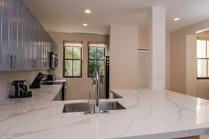 Modern kitchen with marble countertops, stainless steel sink, and large windows.