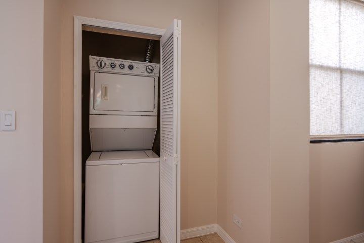Stacked washer and dryer in a narrow closet with open white louvered doors.