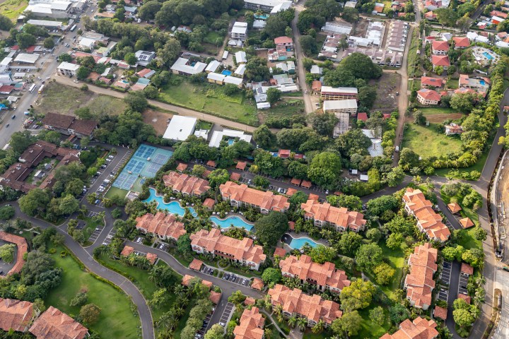 Aerial view of a coastal town with green areas and red-roofed buildings near the sea.