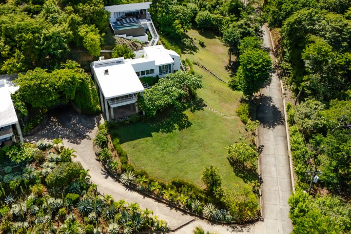 Aerial view of modern houses surrounded by lush greenery and a winding road.