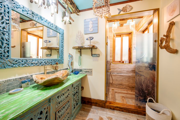 Bathroom with nautical decor, green vanity with seashell sink, and open shower with wooden accents.
