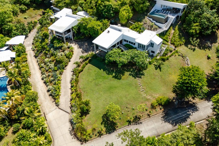 Aerial view of modern white houses with gardens and pathways surrounded by lush greenery.