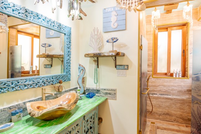 Colorful bathroom with wooden sink, blue accents, shell light fixture, and beach-themed decor.