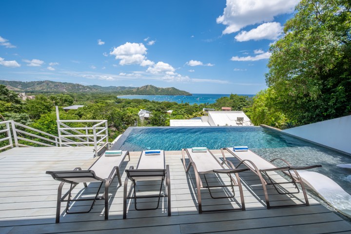 Infinity pool with four lounge chairs overlooking a scenic view of ocean and islands.