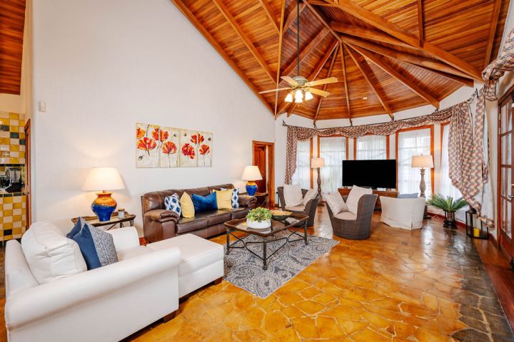 Spacious living room with high wooden ceiling, sofas, TV, and decorative pillows.