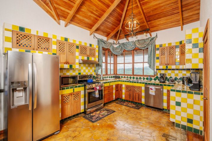Rustic kitchen with wooden cabinets, yellow-green tiles, stainless appliances, and a wooden ceiling.