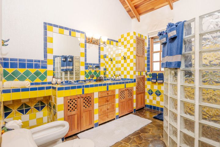 Colorful bathroom with yellow, blue tiles, wooden cabinets, glass block wall, and blue towels.