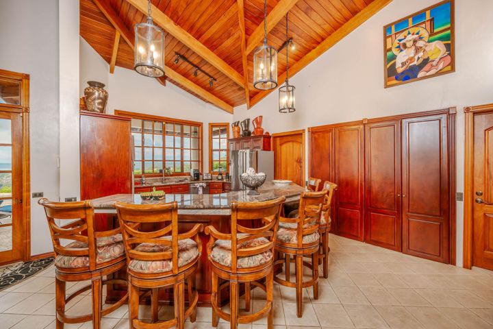 Spacious kitchen with wooden ceiling, bar stools, and pendant lights over a central island.