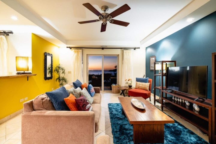 Cozy living room with colorful cushions, yellow accent wall, and sliding doors to a sunset view.