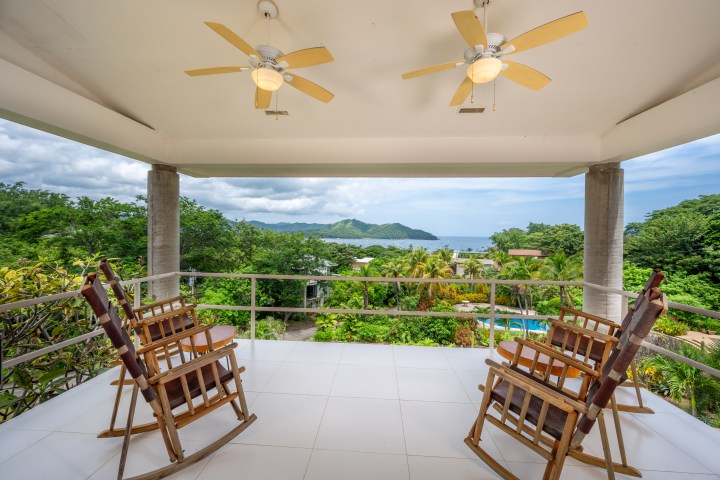 Balcony with two rocking chairs, ceiling fans, and ocean view in the distance.