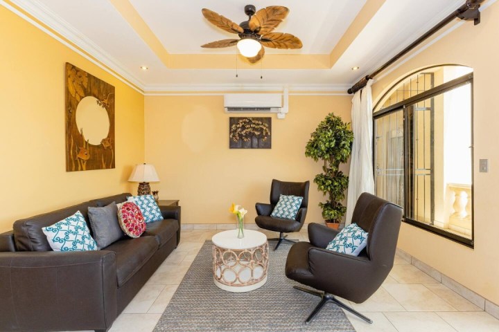 Cozy living room with yellow walls, brown sofa, armchairs, round table, and ceiling fan.