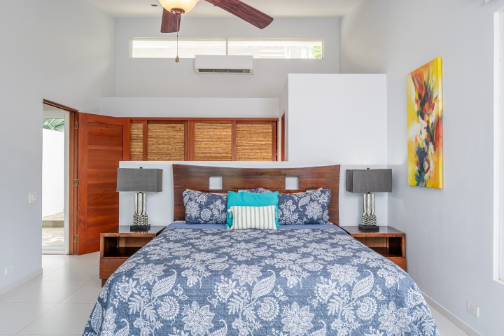 Modern bedroom with wooden furniture, floral bedspread, and colorful abstract painting on the wall.