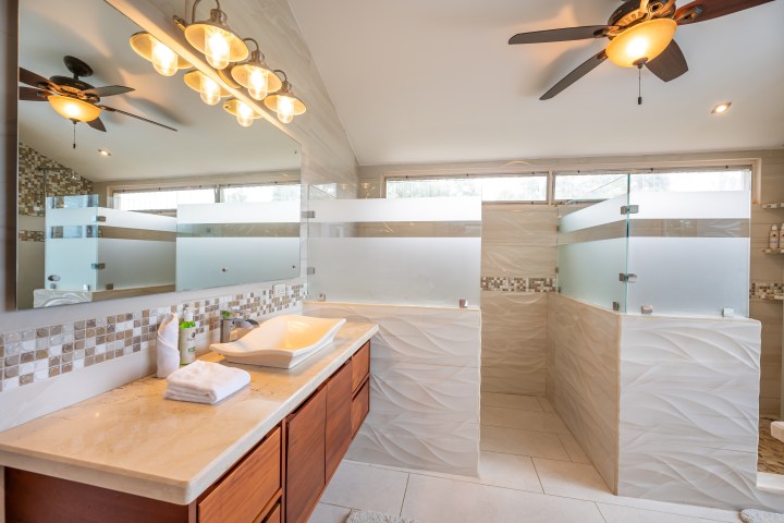 Modern bathroom with dual sinks, large mirror, glass shower partitions, and ceiling fans.