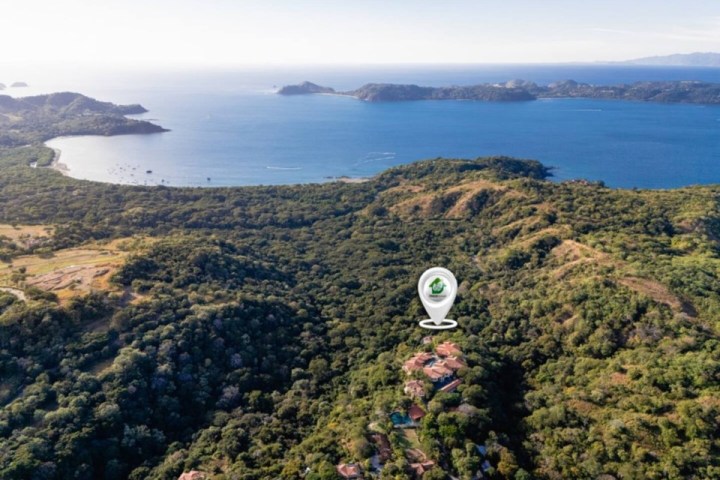 Aerial view of coastline with hills and water. Map pin marks a location in a forested area.