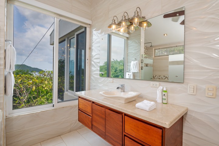 Bathroom with large mirror, wooden vanity, and view of trees and sky through window.
