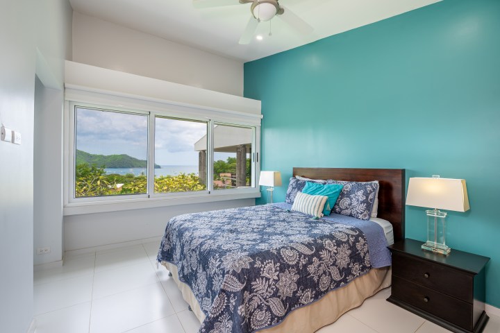 Bedroom with blue accent wall, large window with ocean view, and bed with floral bedding.