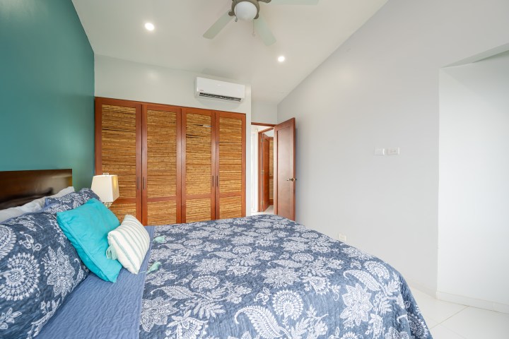 Bedroom with a blue floral bedspread, wooden closet, and white walls.