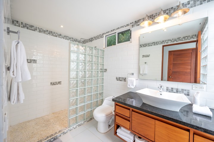 Modern bathroom with glass wall shower, wooden cabinet, sink, and large mirror above.
