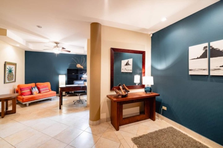 Living room with orange couch, dark blue accent wall, mirror, and desk.