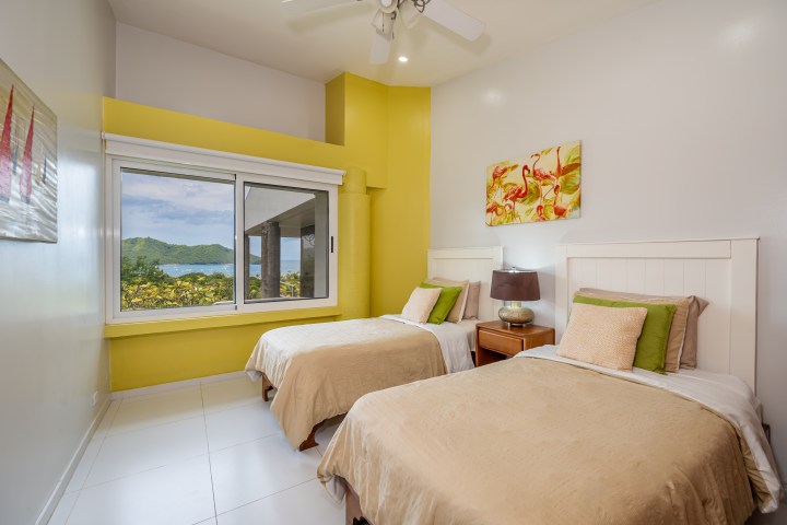 Bright bedroom with two twin beds, window view of trees and ocean, and flamingo artwork.
