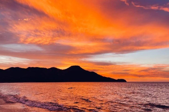 Vivid orange sunset over ocean waves with a silhouette of a mountain.