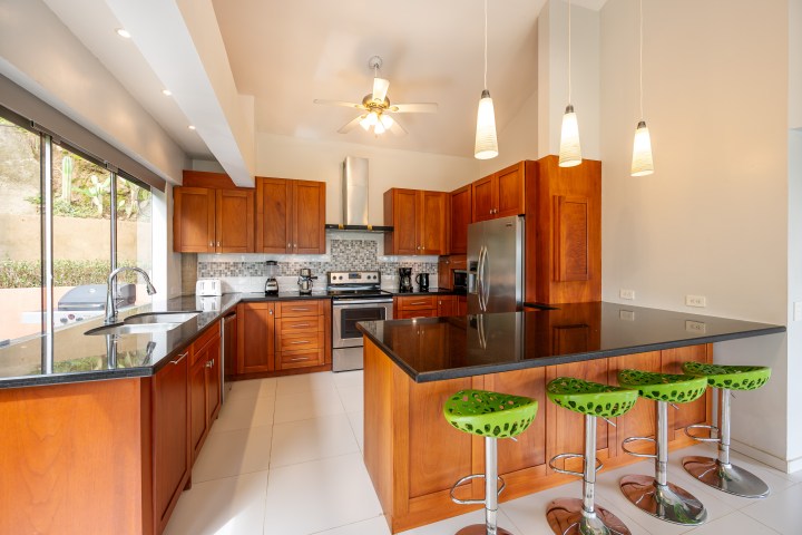 Modern kitchen with wooden cabinets, stainless steel appliances, and green barstools at black countertop island.
